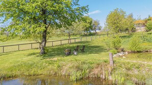 A grassy area with a pond, wooden benches, and a fence. - Organic Homestead Mikl Spruce Tree Apt, Slovenj Gradec, Slovenia (Slovenj Gradec)