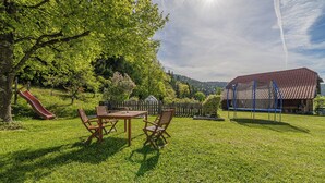 A grassy outdoor area with a picnic table and chairs, a slide, a fenced play area, and a building with a red roof. - Organic Homestead Mikl Spruce Tree Apt, Slovenj Gradec, Slovenia (Slovenj Gradec)