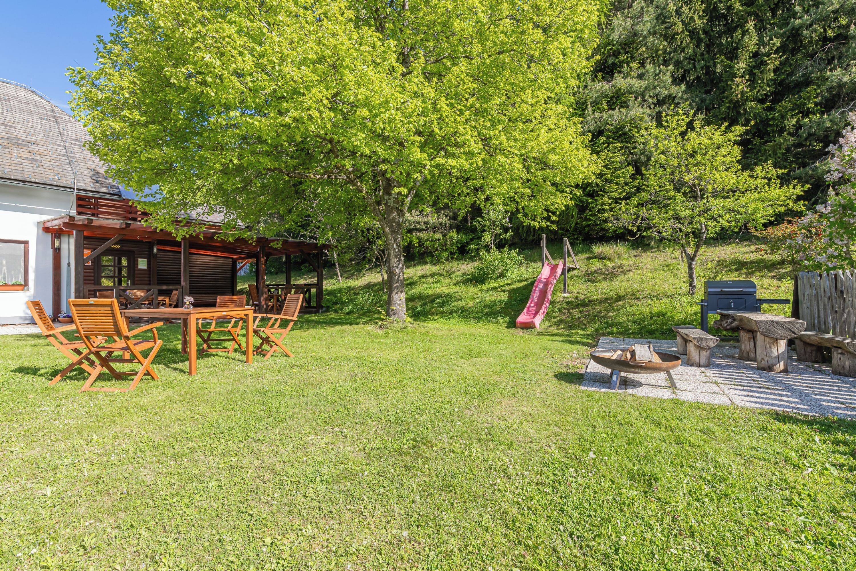 A backyard with a wooden table and chairs, a fire pit, and a slide.