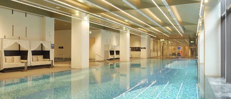 A long indoor swimming pool with clear water, surrounded by white walls and columns, and equipped with modern lighting fixtures.