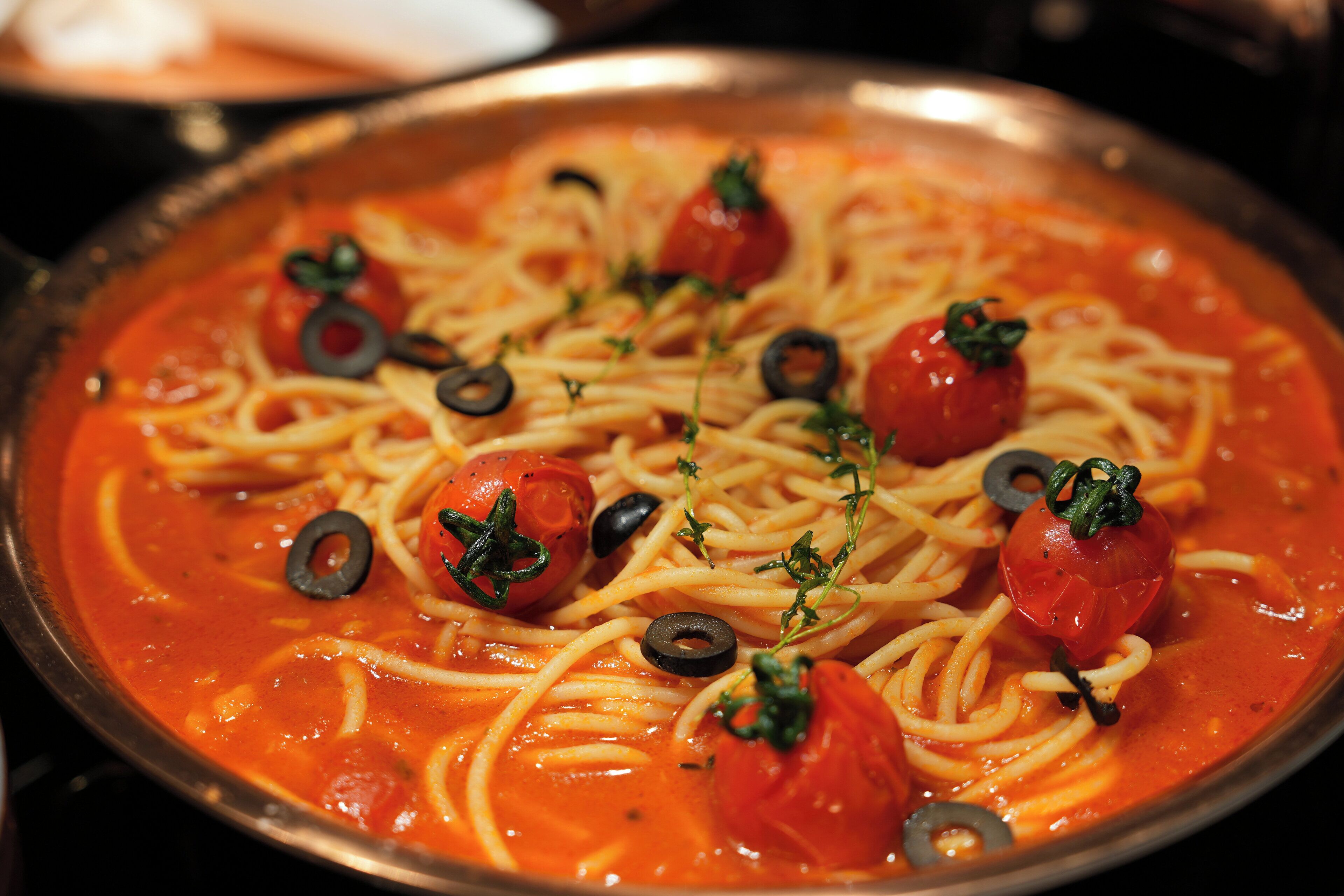 A dish of spaghetti with cherry tomatoes and black olives.