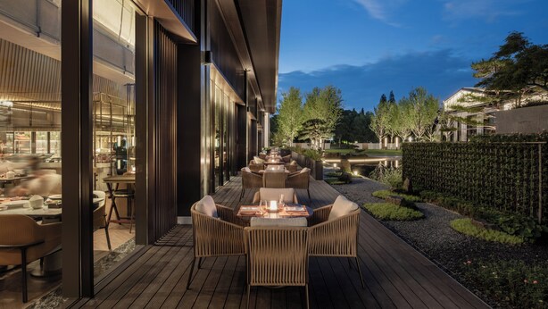 An outdoor dining area with a long table and chairs, surrounded by a wooden deck and a garden. - Intercontinental Xiangyang by IHG (Xiangyang)