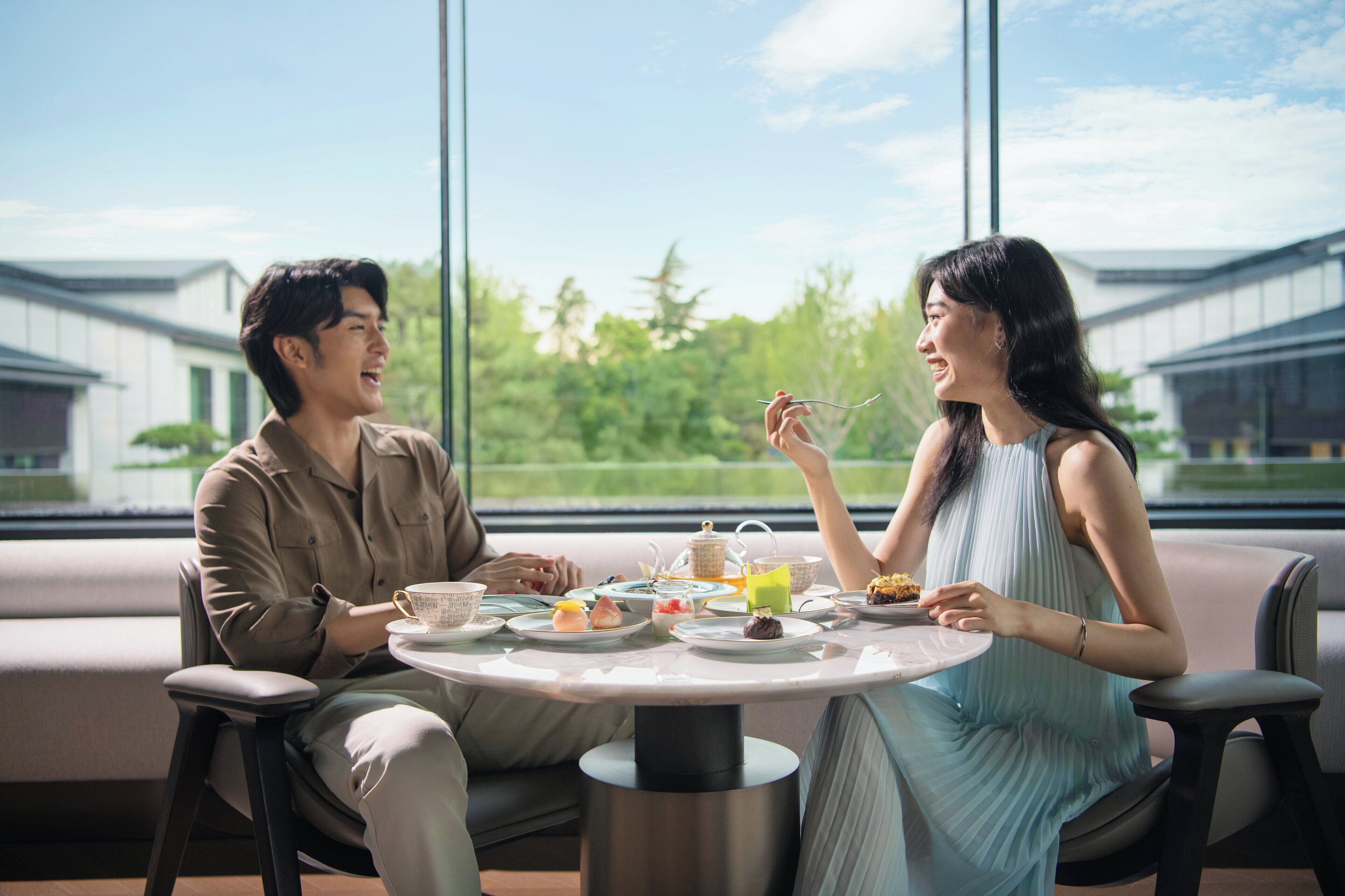 Un couple est assis à une table, profitant d’une vue sur des bâtiments traditionnels et la verdure environnante.
