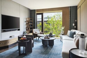 A modern living room with a flat-screen TV, a sofa, two armchairs, a coffee table, and a bookshelf.
