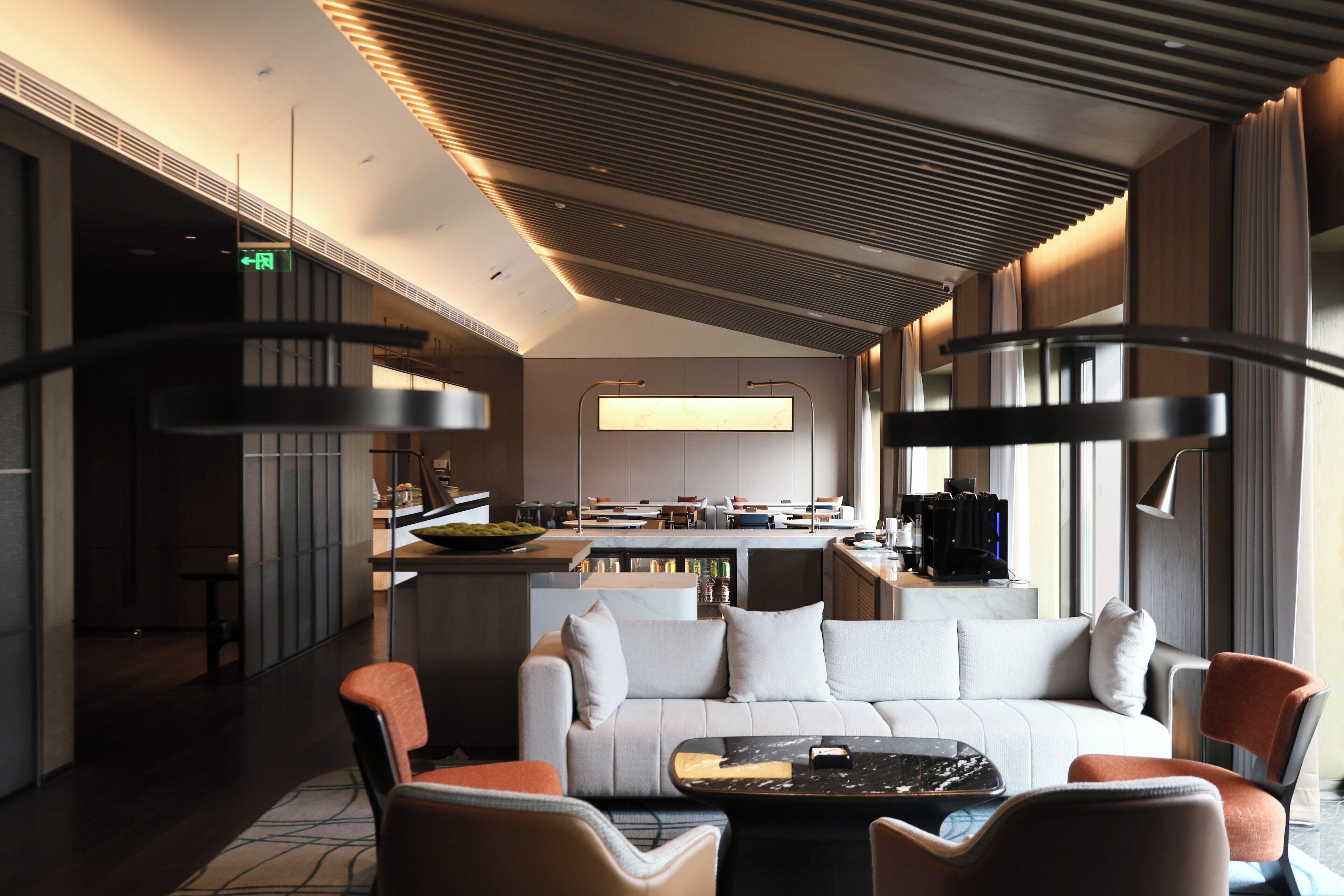 Eine moderne Hotelhalle mit einer Couch, Sesseln, einem Couchtisch und einer Küchenzeile im Hintergrund.