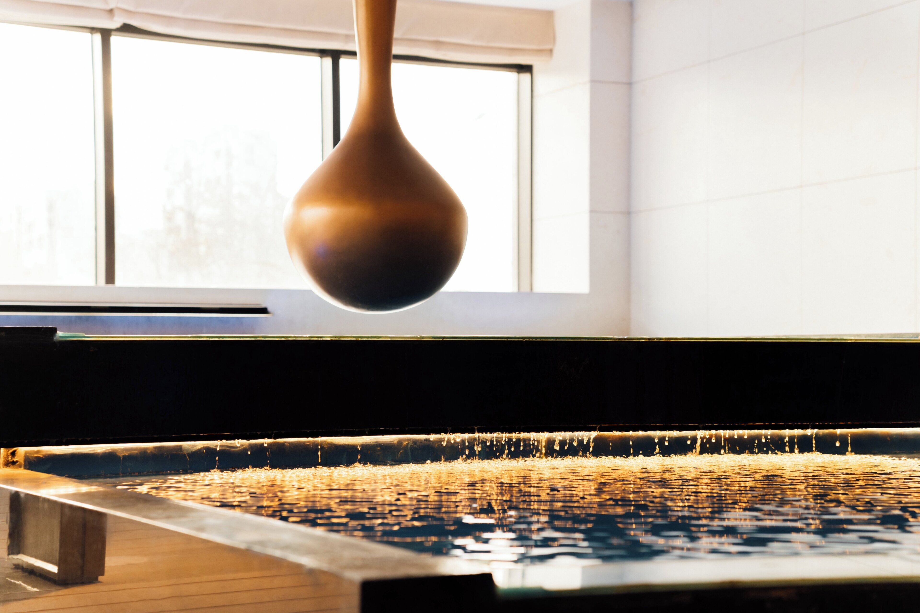 A close-up of a water feature with a hanging object, possibly a decorative element, in a room with a window and tiled walls.