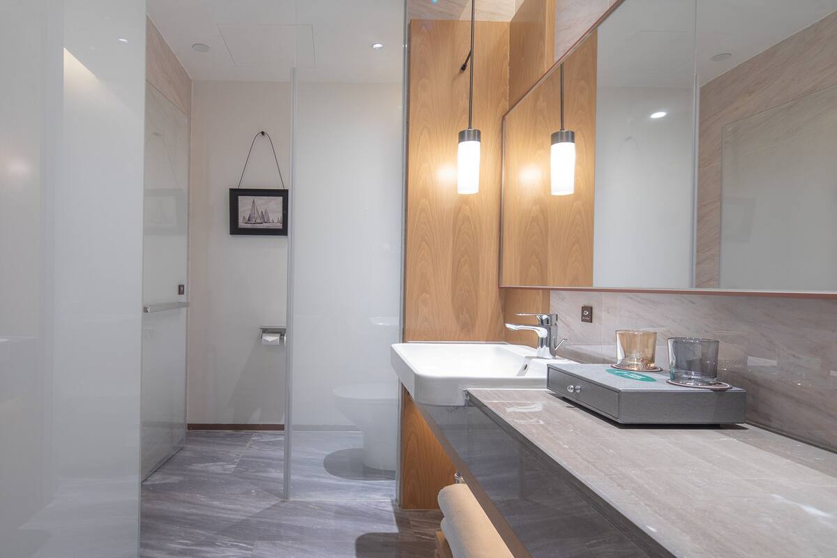 Een moderne badkamer met een douchecabine van glas, een houten wastafelmeubel met een wastafel en een grote spiegel.