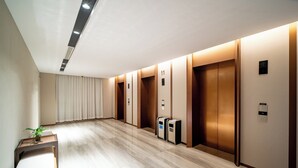 A modern hallway with wooden floors, numbered elevator doors, and a small table with a plant. - Holiday Inn Ningbo Xianshan Damu Bay by IHG (Ningbo)