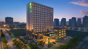 A high-rise hotel with a prominent green logo, multiple floors, and a well-lit entrance area. - Holiday Inn Ningbo Xianshan Damu Bay by IHG (Ningbo)