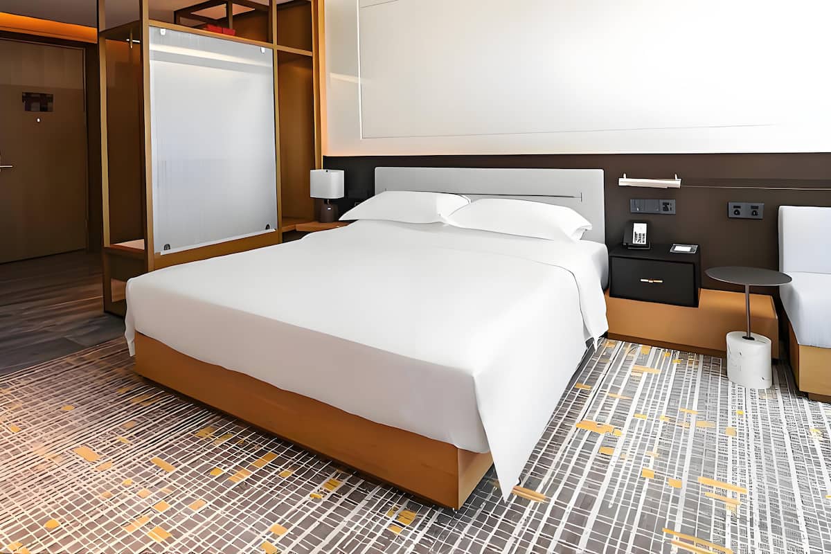 Een hotelkamer met een groot bed, een kledingkast, een nachtkastje met lamp en een kleine tafel met stoel.
