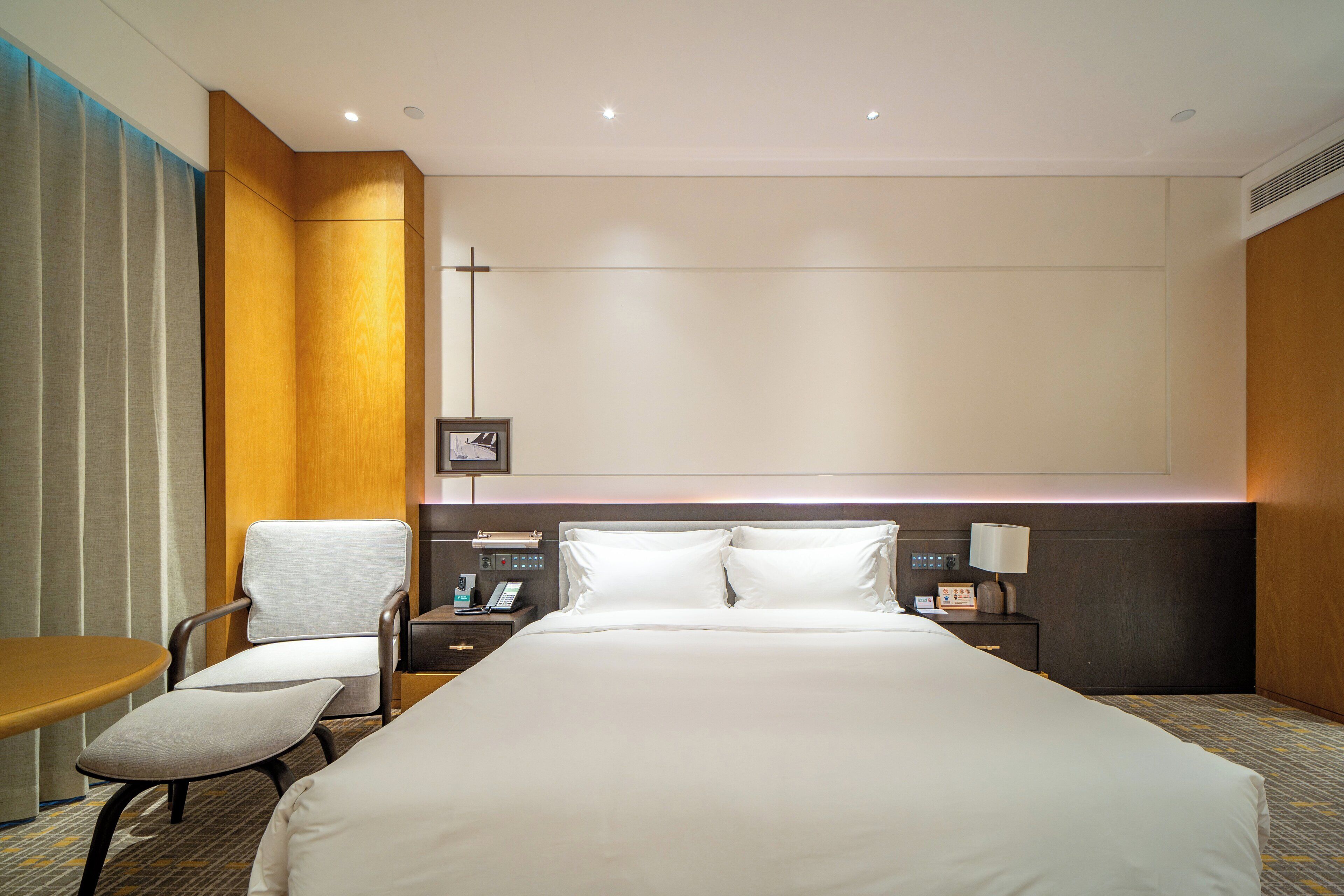 A hotel room with a large bed, a bedside table with a lamp, a chair, and a small table.