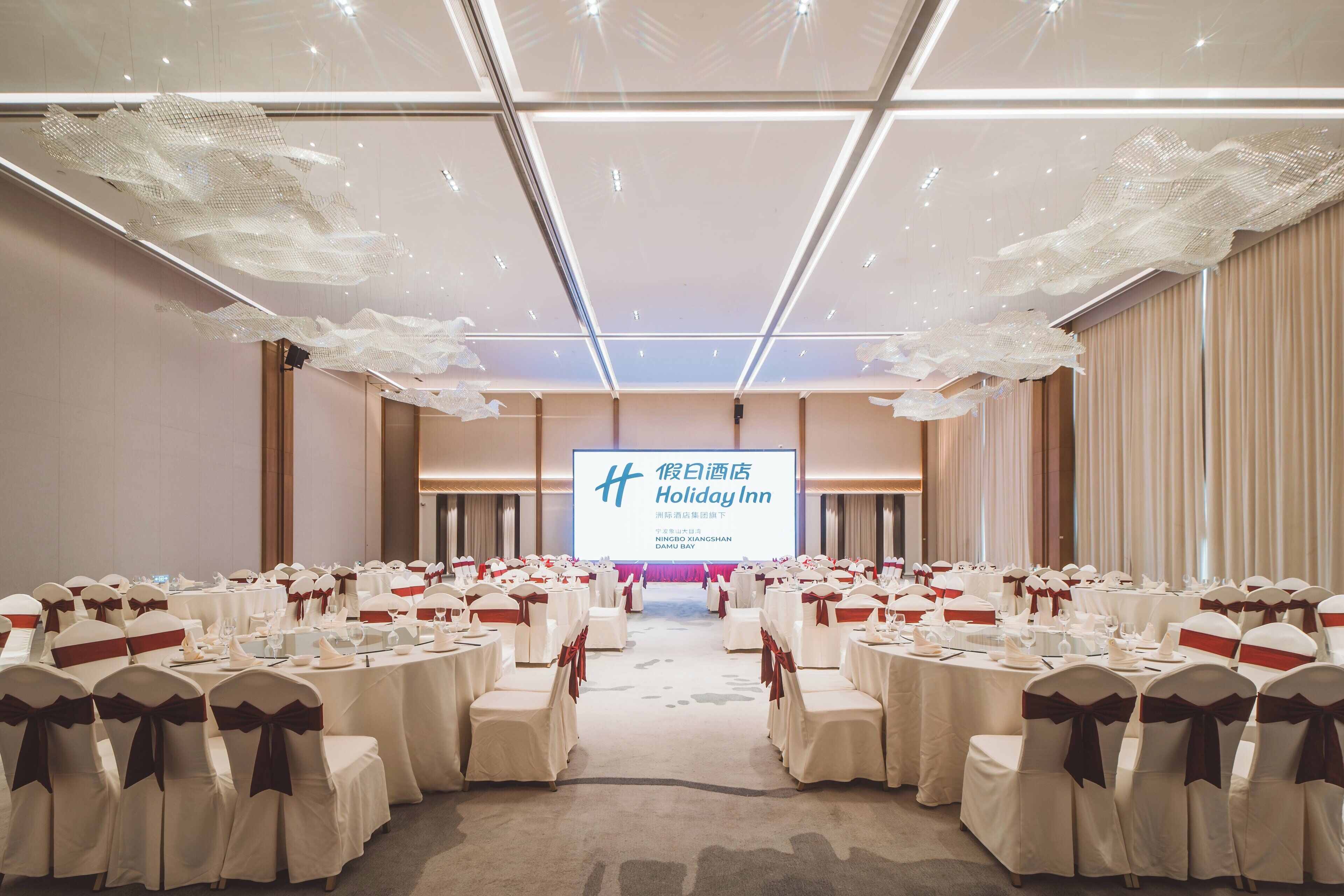 A conference room with rows of tables and chairs, a large screen at the front, and a stage area.