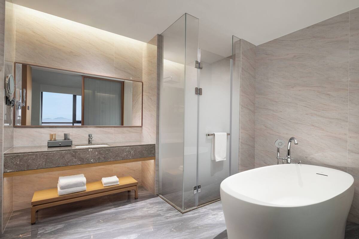 Een moderne badkamer met een groot bad, een douche met glazen wand, een wastafel met spiegel en een bankje.