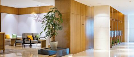 A modern lobby with a seating area, a large potted plant, and a reception desk.