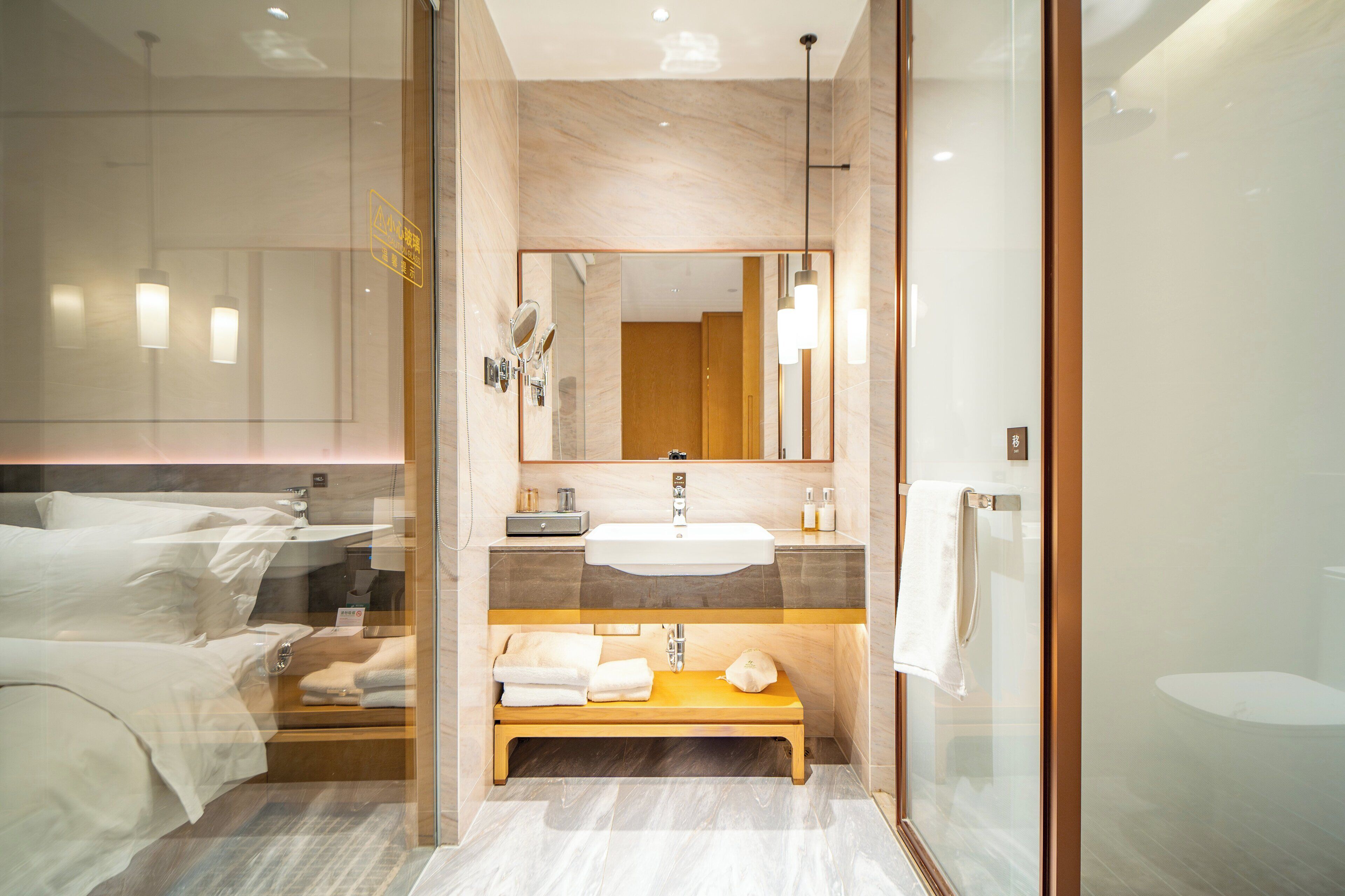 A modern bathroom with a glass shower enclosure, a wooden bench, a large mirror, and a sink with a vanity.