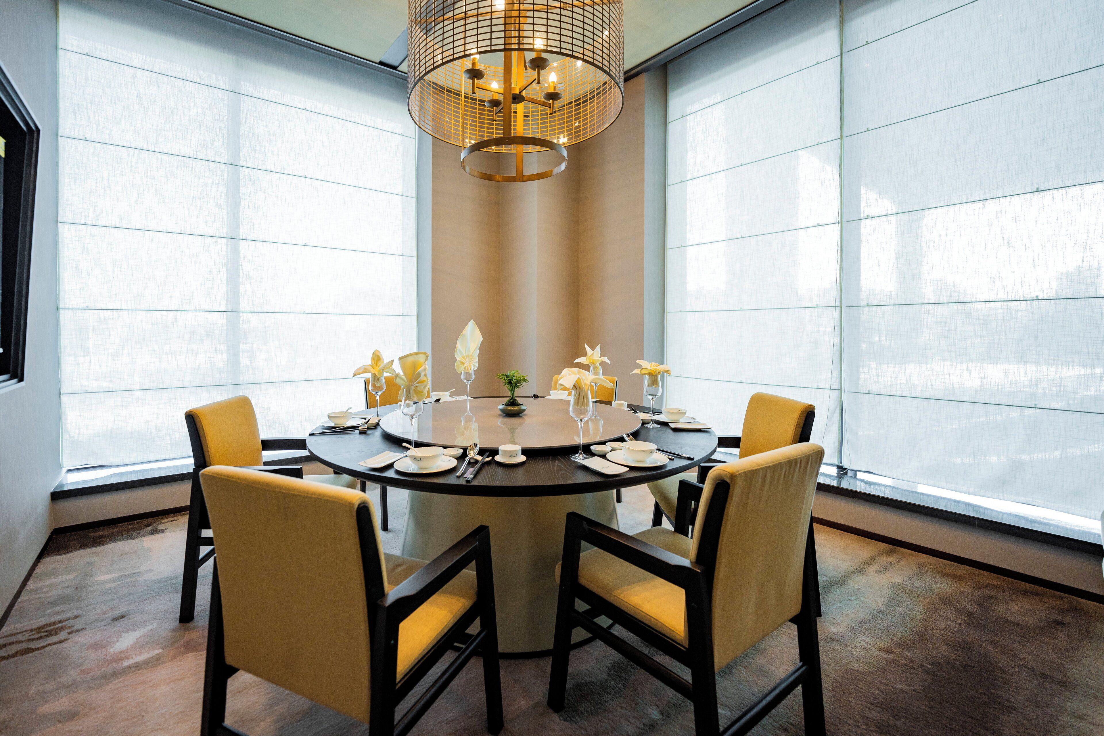A round dining table with chairs, a chandelier, and a view through large windows.