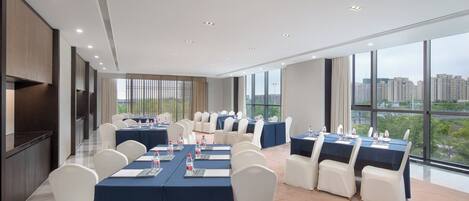A conference room with tables and chairs, large windows, and a city view.