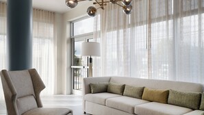 Una sala moderna con un sofá seccional, un sillón y un ventanal con cortinas translúcidas.