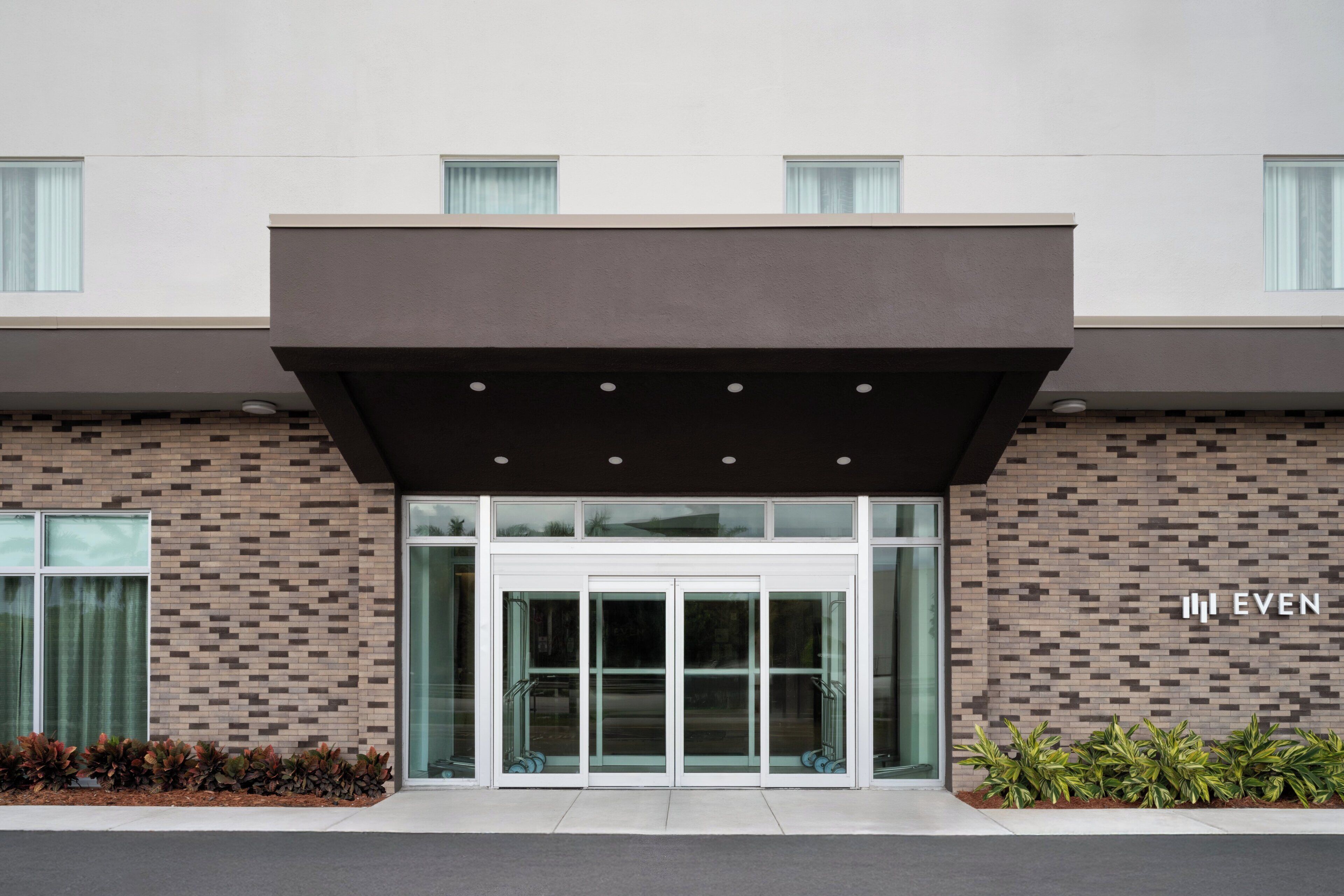 Un bâtiment moderne avec une façade en briques, de grandes portes d’entrée en verre et une enseigne indiquant le mot « EVEN ».