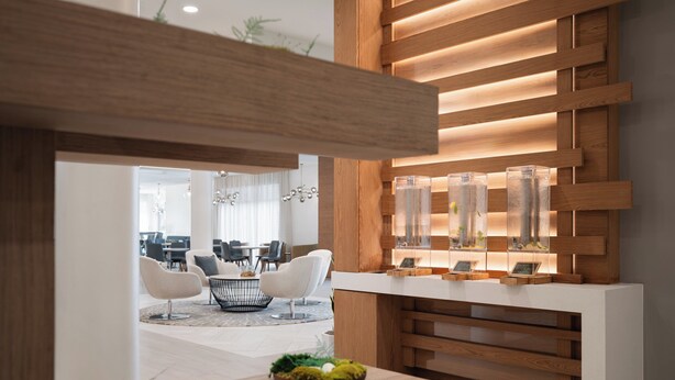 Un interior moderno con un mostrador de recepción de madera, vitrinas de vidrio y un área de descanso con sillas blancas.