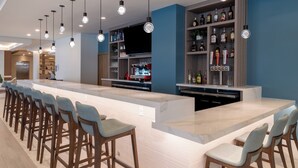Un área de bar moderna con una barra larga, taburetes y estantes llenos de botellas.