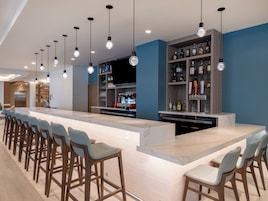 Un área de bar moderna con una barra larga, taburetes y estantes llenos de botellas.