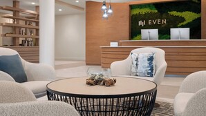 Una moderna zona de recepción con un mostrador de madera, una mesa redonda con elementos decorativos y un espacio de estar con sofás.