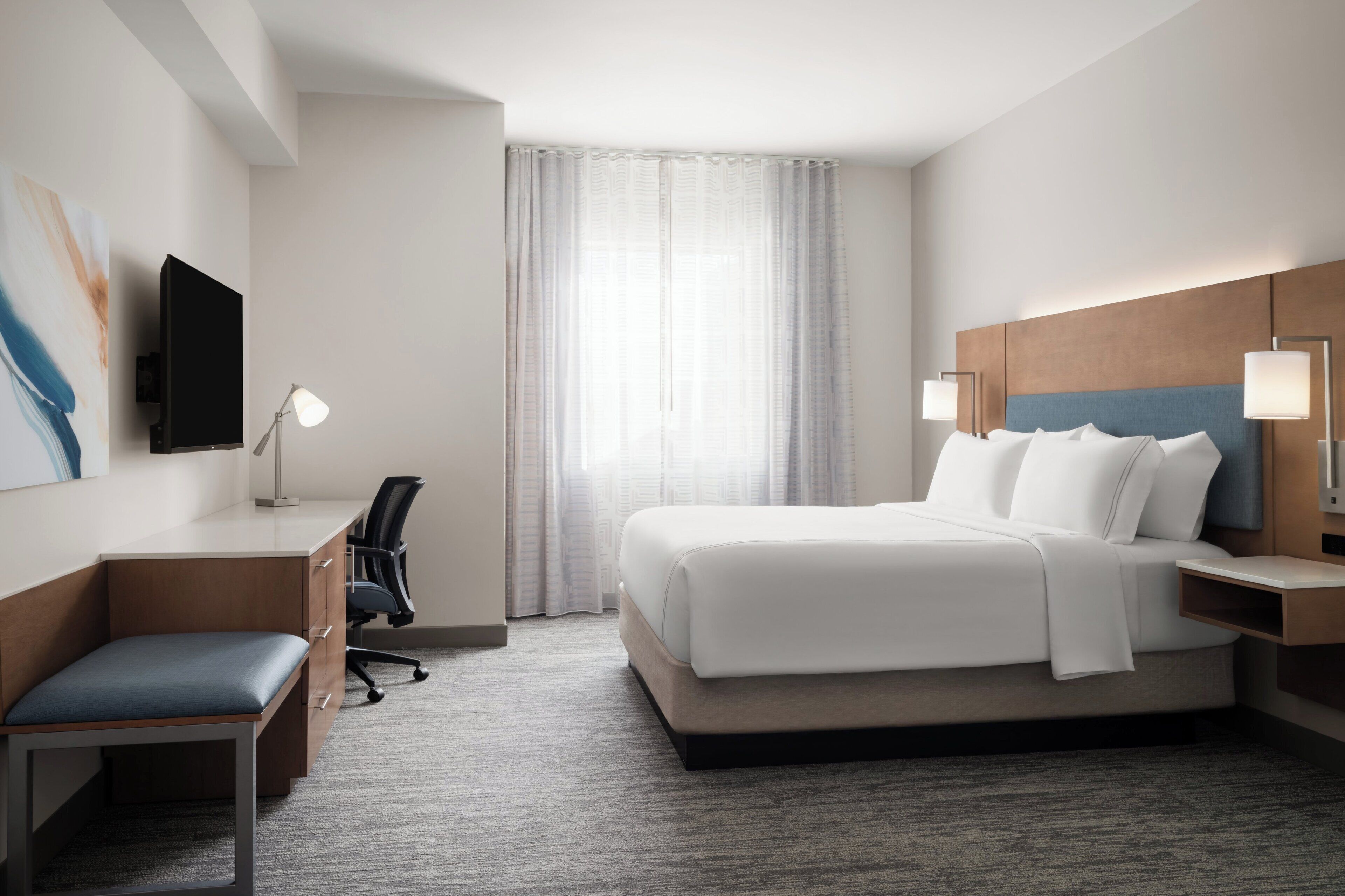 A hotel room with a bed, desk, chair, and a television.
