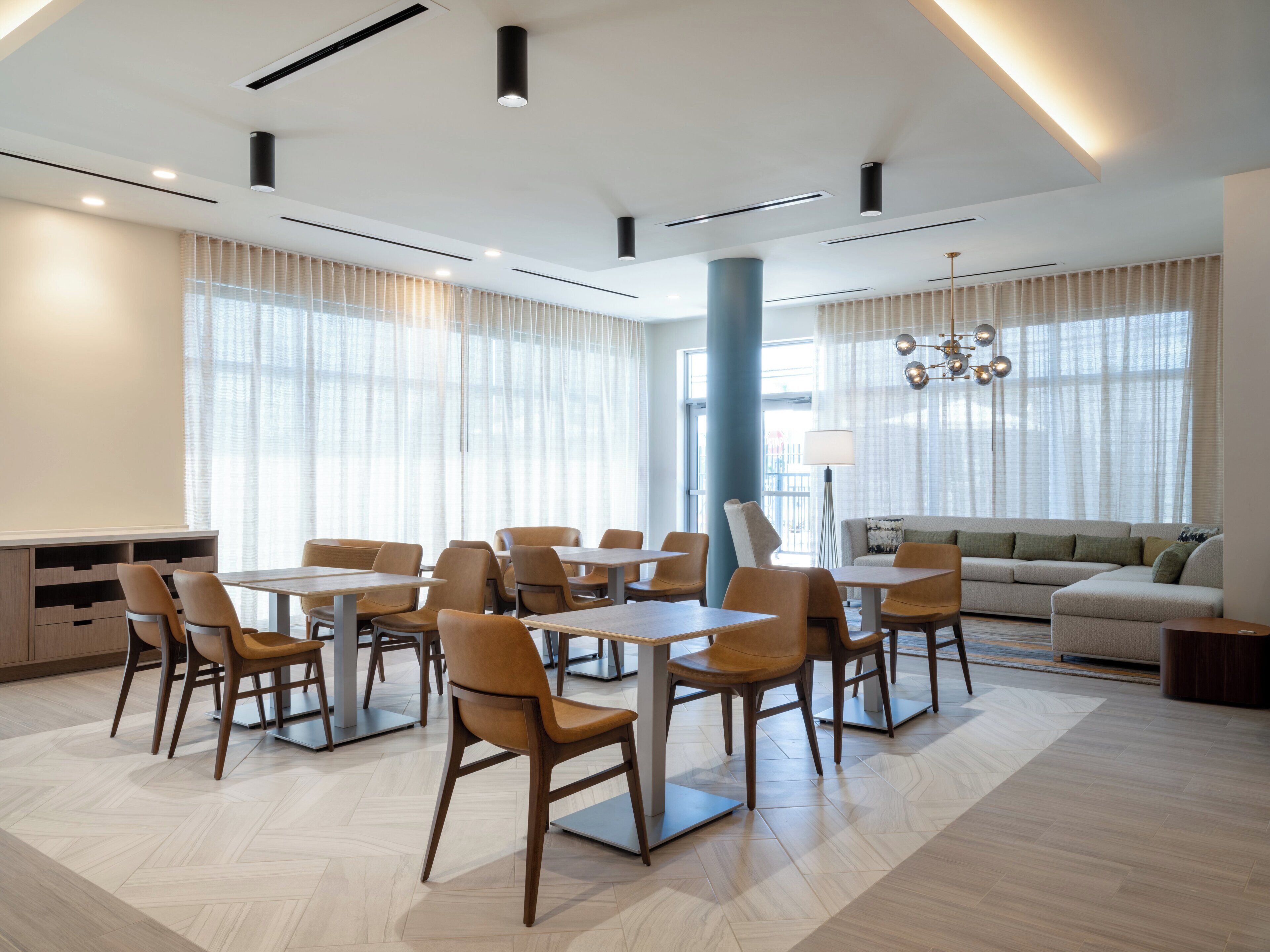 Une chambre d’hôtel moderne dotée d’un coin repas, d’un canapé et d’une grande fenêtre avec des rideaux.