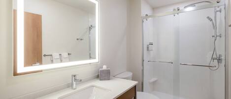 A modern bathroom with a large mirror, a sink, a toilet, and a glass-enclosed shower.