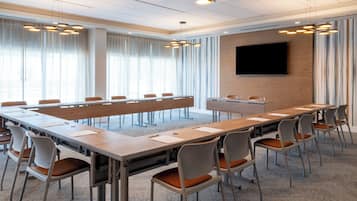 A conference room with a long table, chairs, a flat-screen TV, and a modern chandelier.