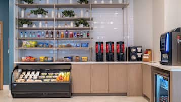 Eine Selbstbedienungs-Getränkestation mit Kaffeeautomat, einem gekühlten Ausstellungsbereich für Snacks sowie Regalen mit Wasserflaschen und Snacks.