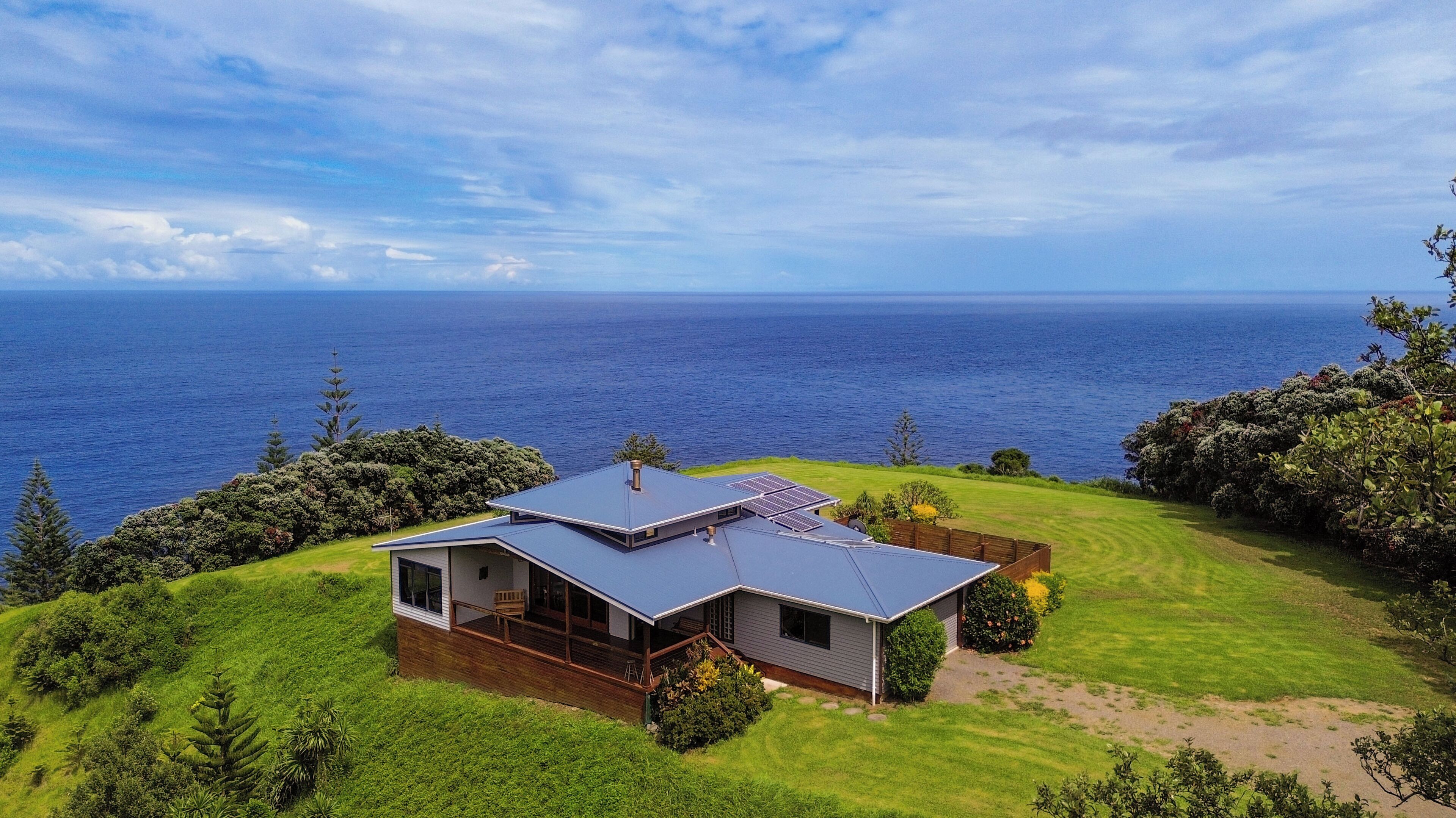 A modern house with a large deck, solar panels, and a view of the ocean.