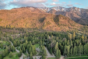 Un paysage montagneux avec une vallée boisée, une route sinueuse et un petit bâtiment doté d’un toit de chaume.