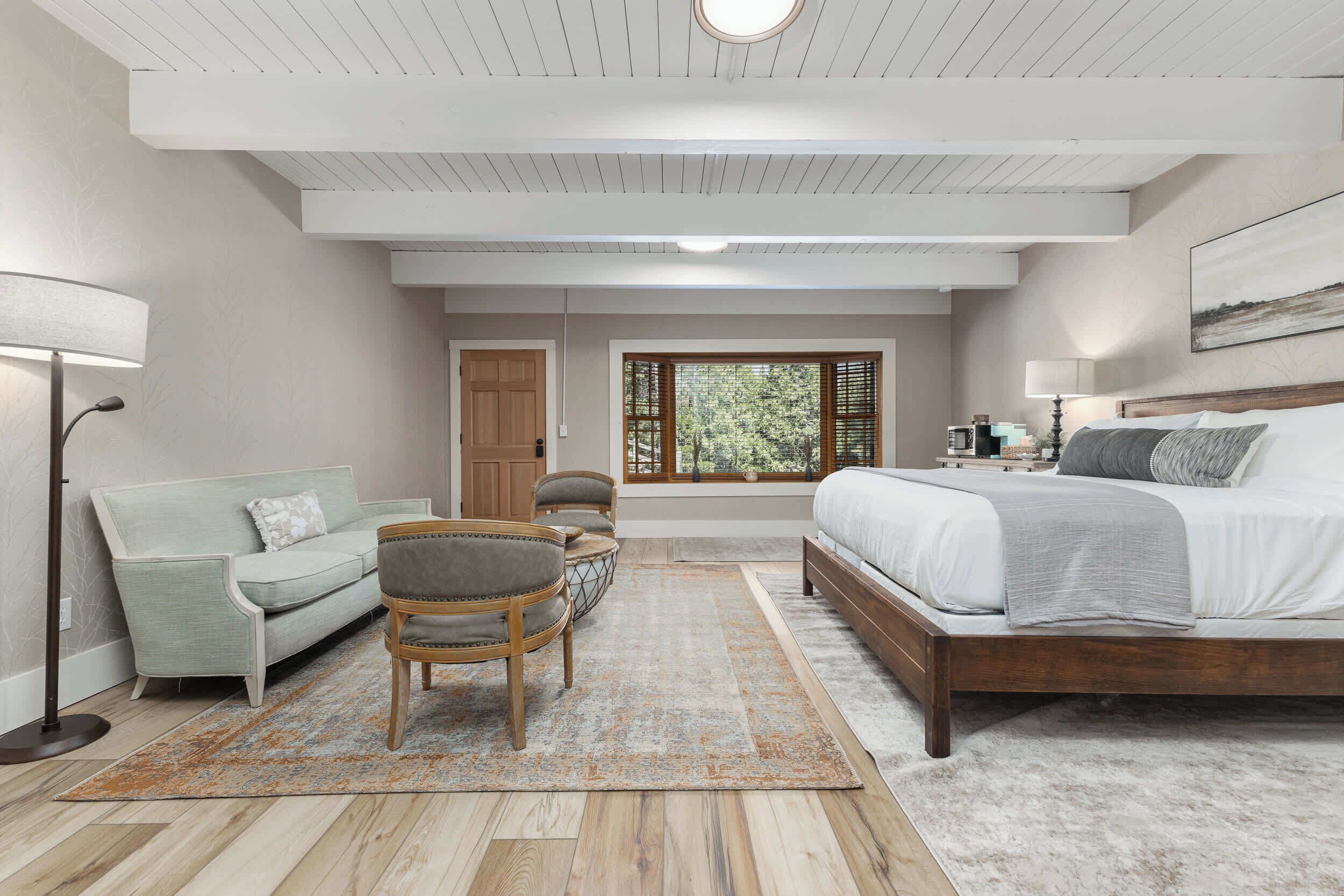 A bedroom with a large bed, a sofa, a chair, and a window with blinds.