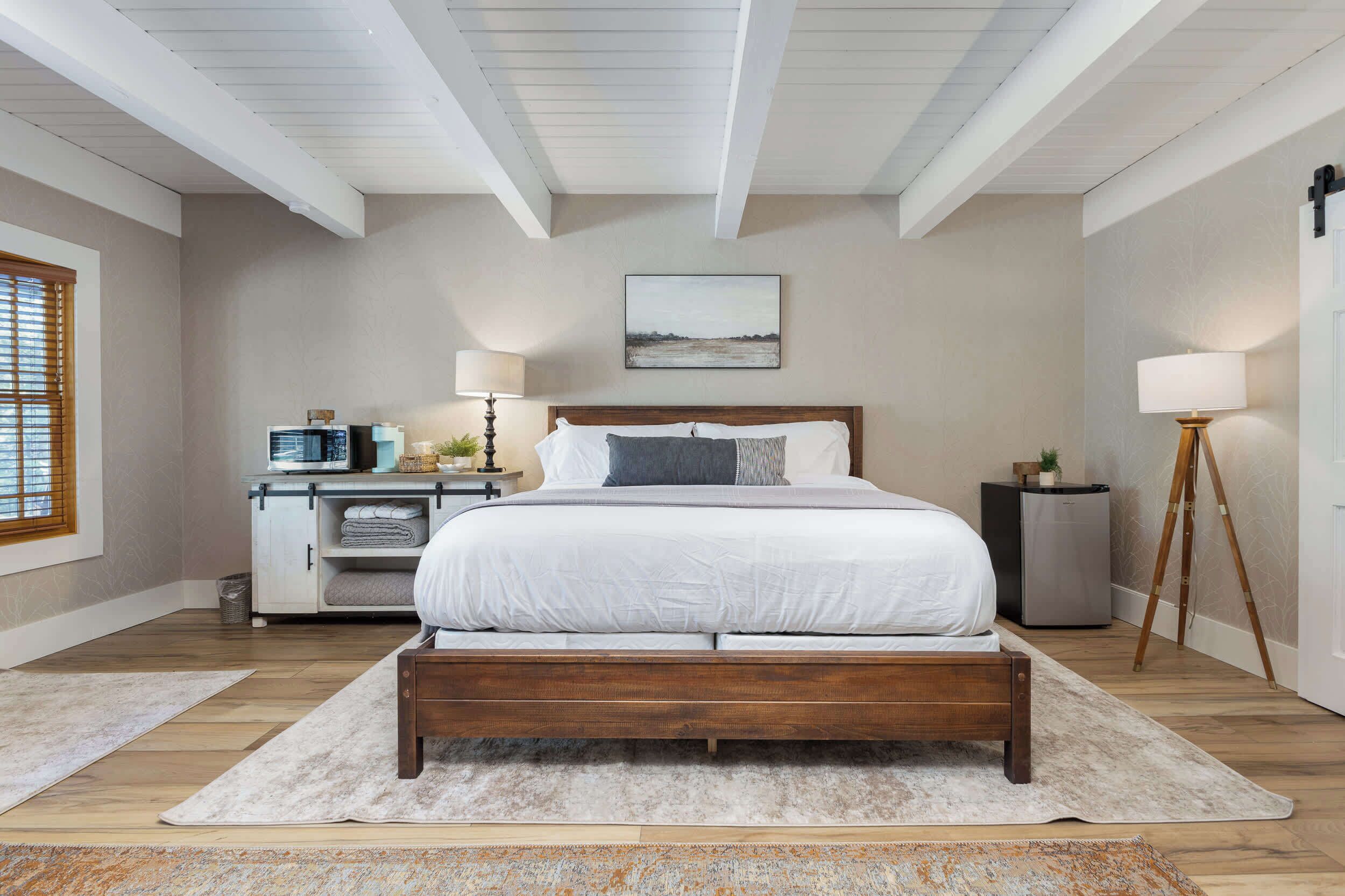 Une chambre à coucher avec un lit en bois, une table de chevet, une lampe et un téléviseur fixé au mur.