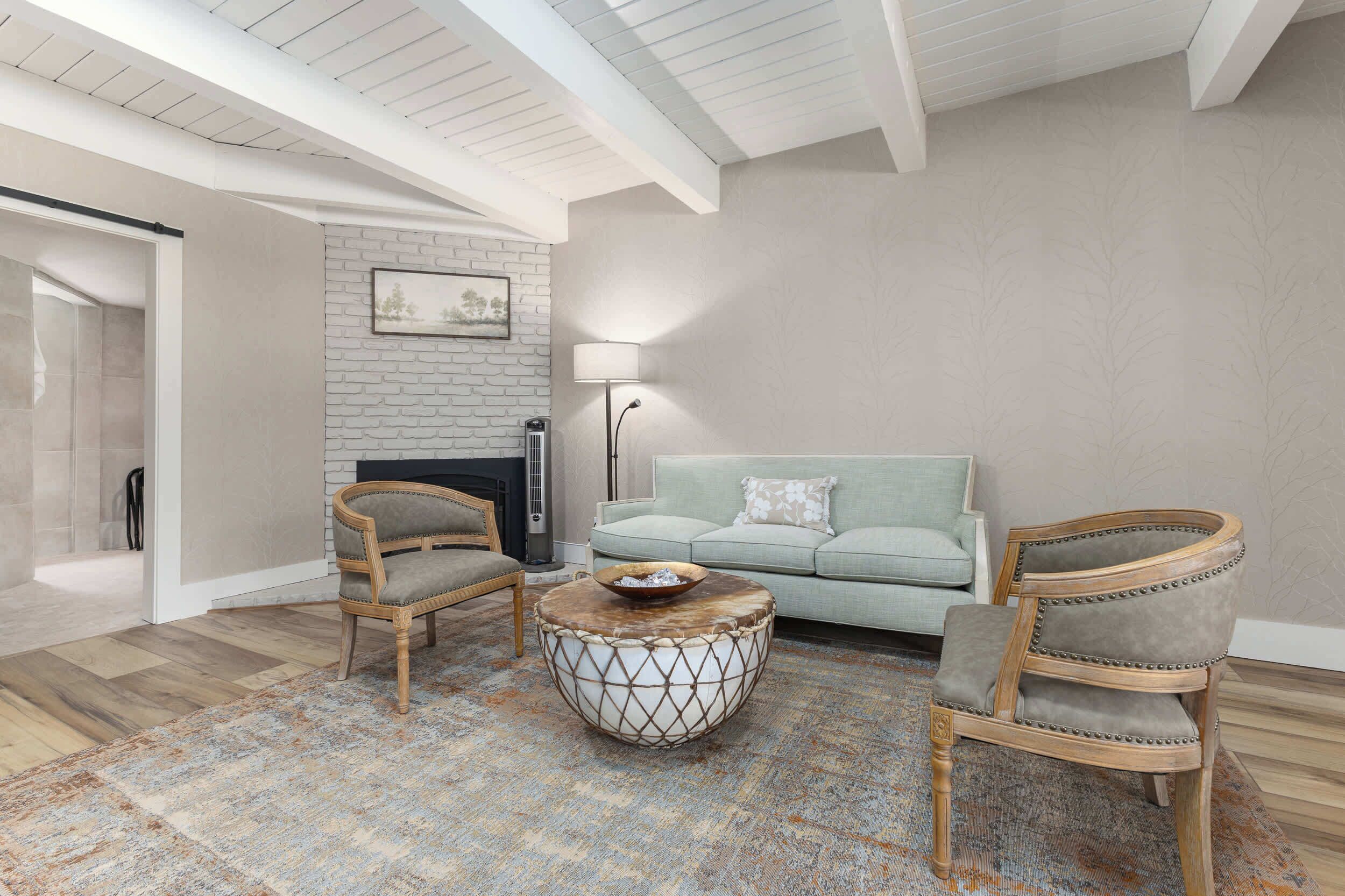 A living room with a fireplace, two armchairs, a sofa, and a patterned rug.