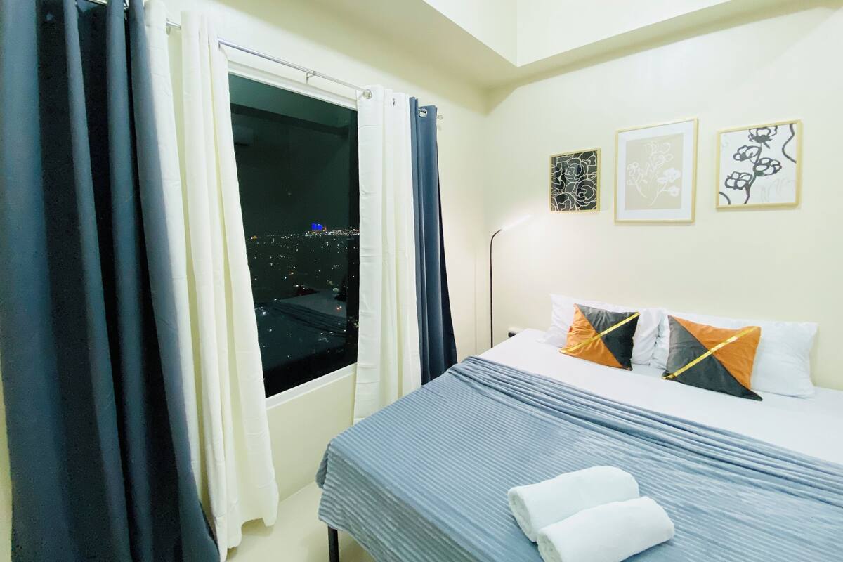 Una habitación de hotel con cama, cortinas, una ventana y decoración en la pared.