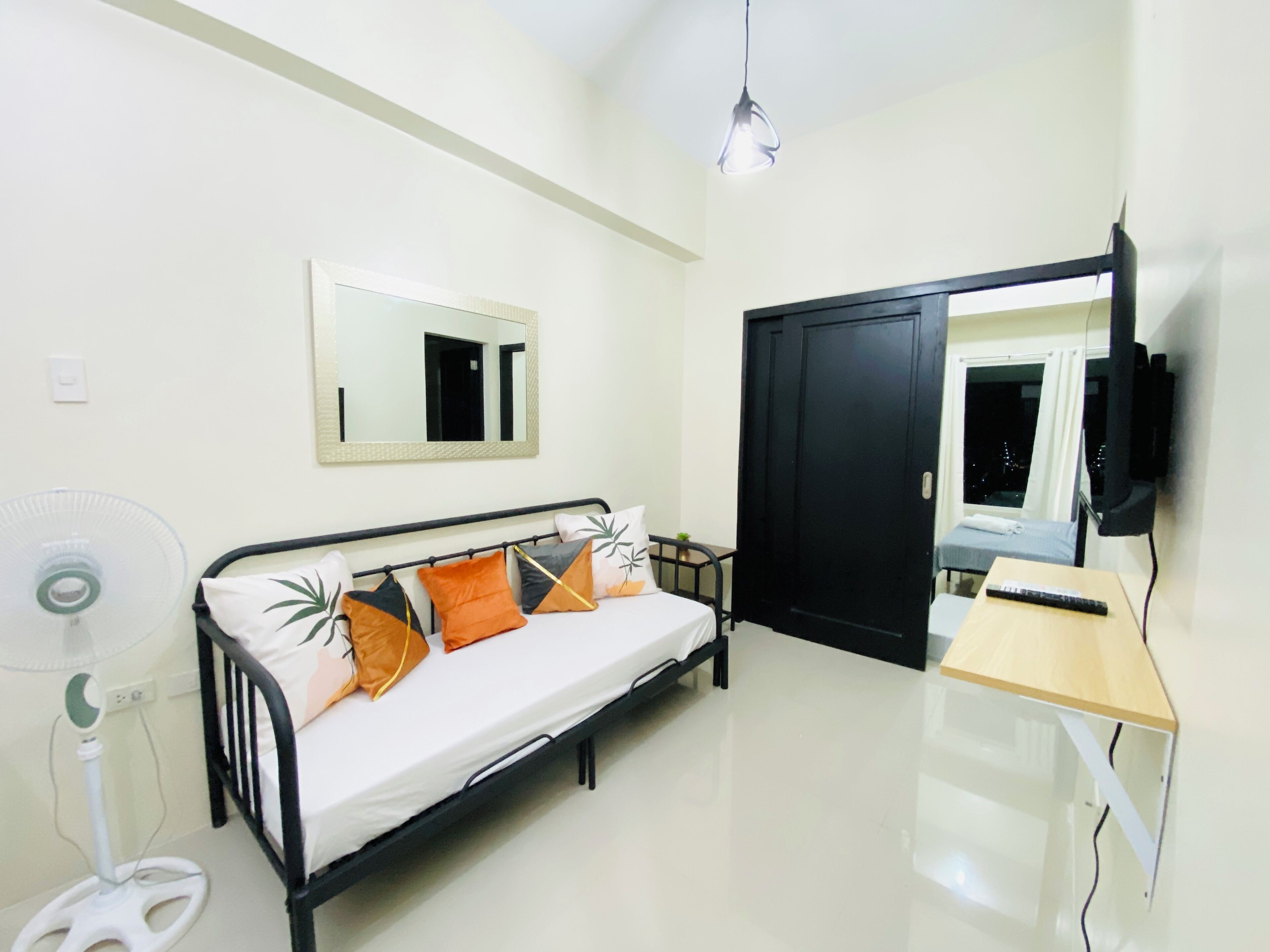 Une chambre d’hôtel de taille réduite, comprenant un lit, une table de chevet, une télévision, un miroir et un ventilateur.