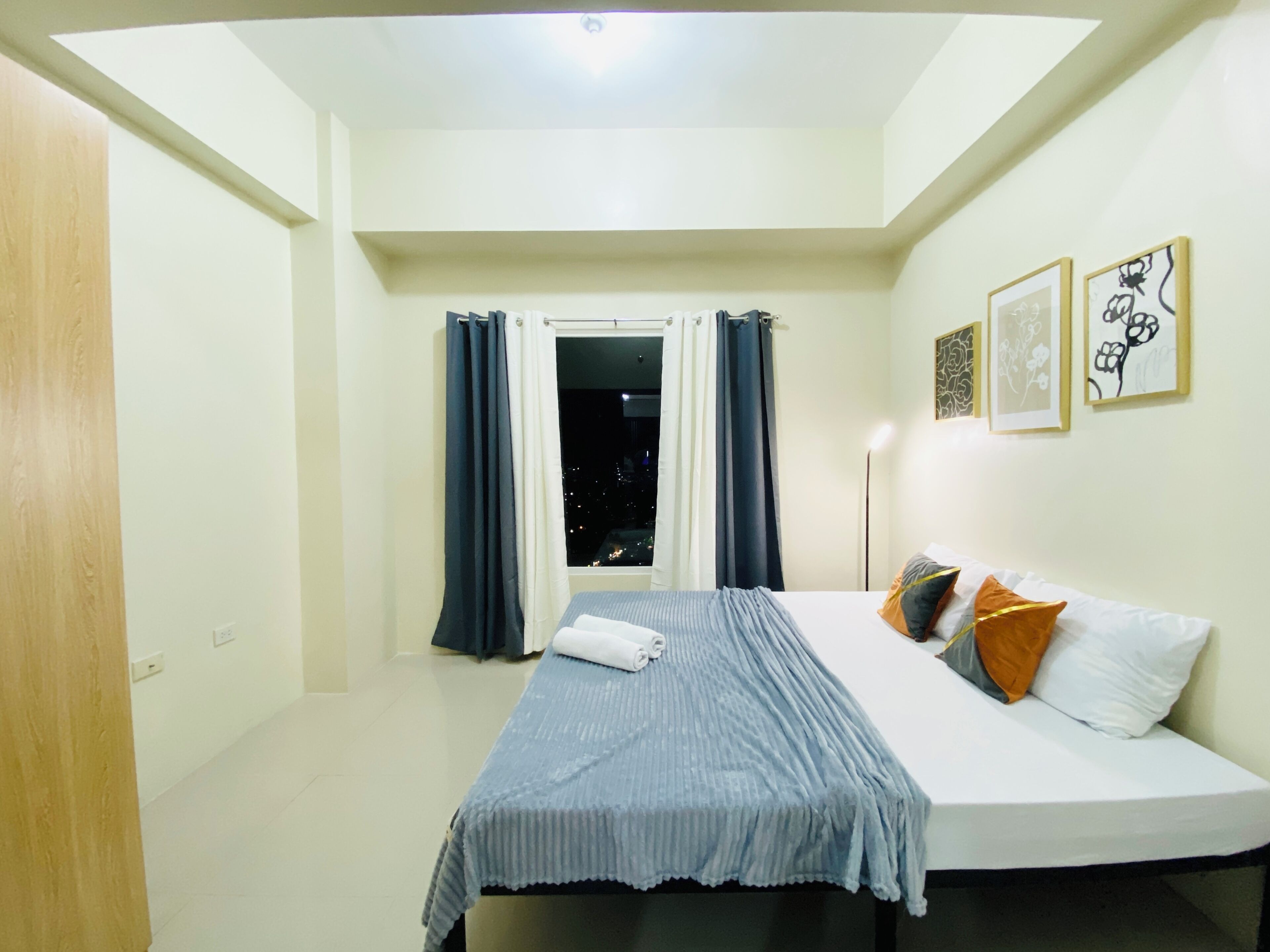 A hotel room with a bed, a window with curtains, and wall art.