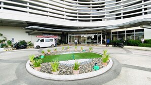 Ein modernes Gebäude mit einer geschwungenen Fassade, einem Parkplatz mit Blumentöpfen und einem weißen Lieferwagen davor.