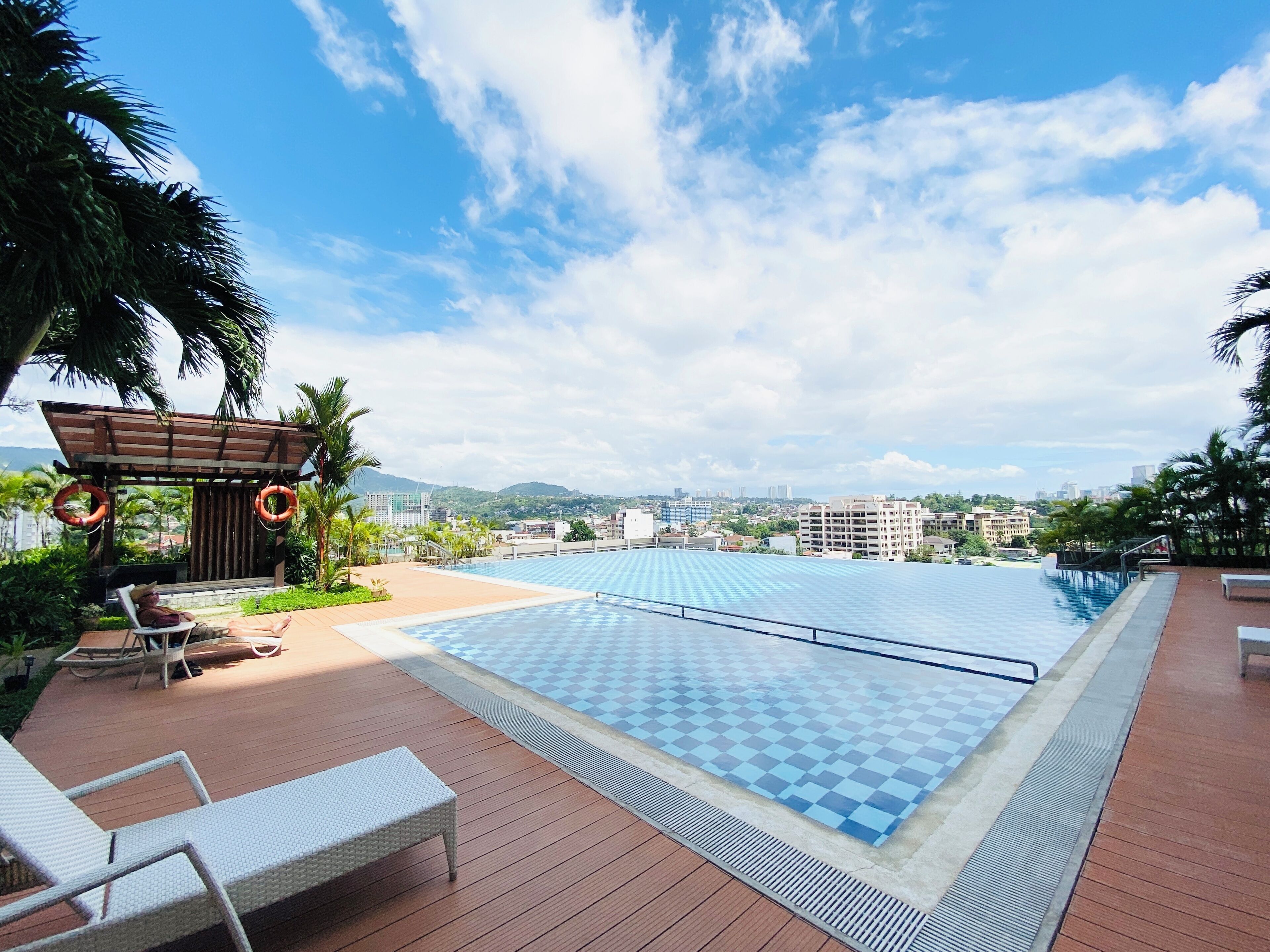 A rooftop pool area with lounge chairs, a pergola, and a view of the cityscape.