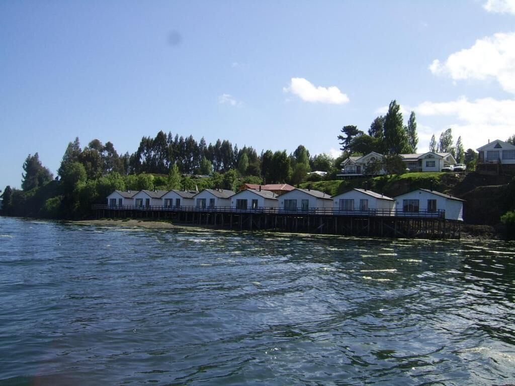 Una propietat a primera línia de mar amb diversos edificis blancs, un moll i un turó cobert de bosc.
