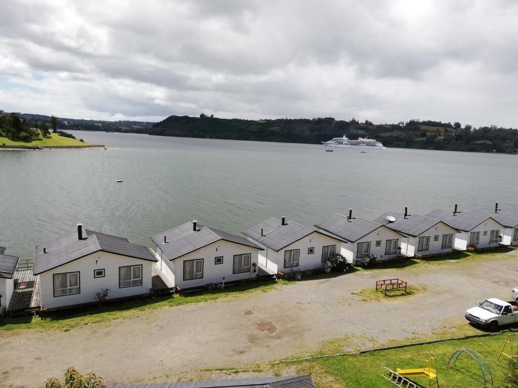 A row of single-story cabins with a view of a lake and a cruise ship in the distance.