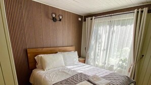 Un letto rifatto con un piumone grigio e bianco, una testiera in legno e un tappeto a righe.