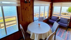 Una baita in legno con un tavolo rotondo e sedie, un divano e ampie finestre che si affacciano su uno specchio d'acqua.