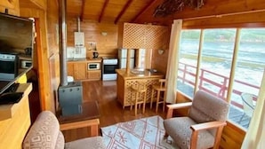 L'interno accogliente di una baita, con arredamento in legno, angolo cottura e zona salotto con tavolo e sedie.