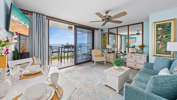 A spacious living room with a balcony, a ceiling fan, and a view of the ocean.