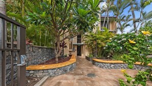 A courtyard with a stone wall, a palm tree, and a building in the background.