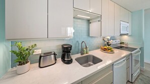 A modern kitchen with white cabinets, a stainless steel toaster, a coffee maker, a sink, and a dishwasher.
